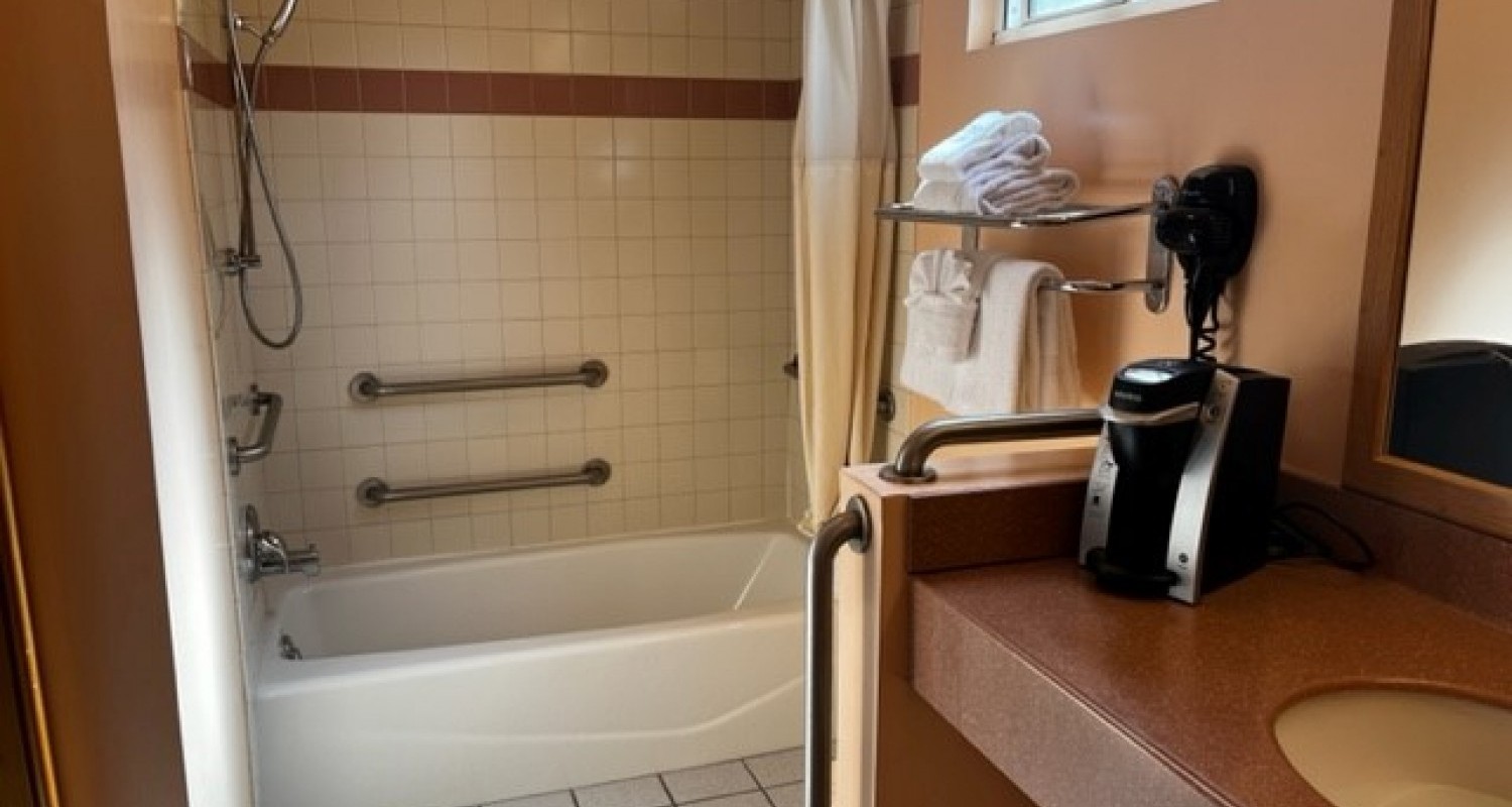 A view of the accessible shower. Has a detachable shower head, and railings inside of the shower.