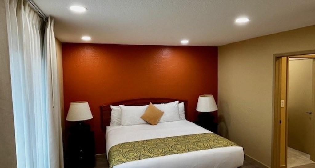 A hotel room with a bed, two nightstands, and a doorway to another room.