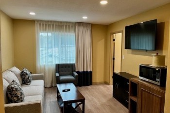 A view of the premium two bedroom suite equipped with a flatscreen TV, table, microwave, luxurious chairs and couch.