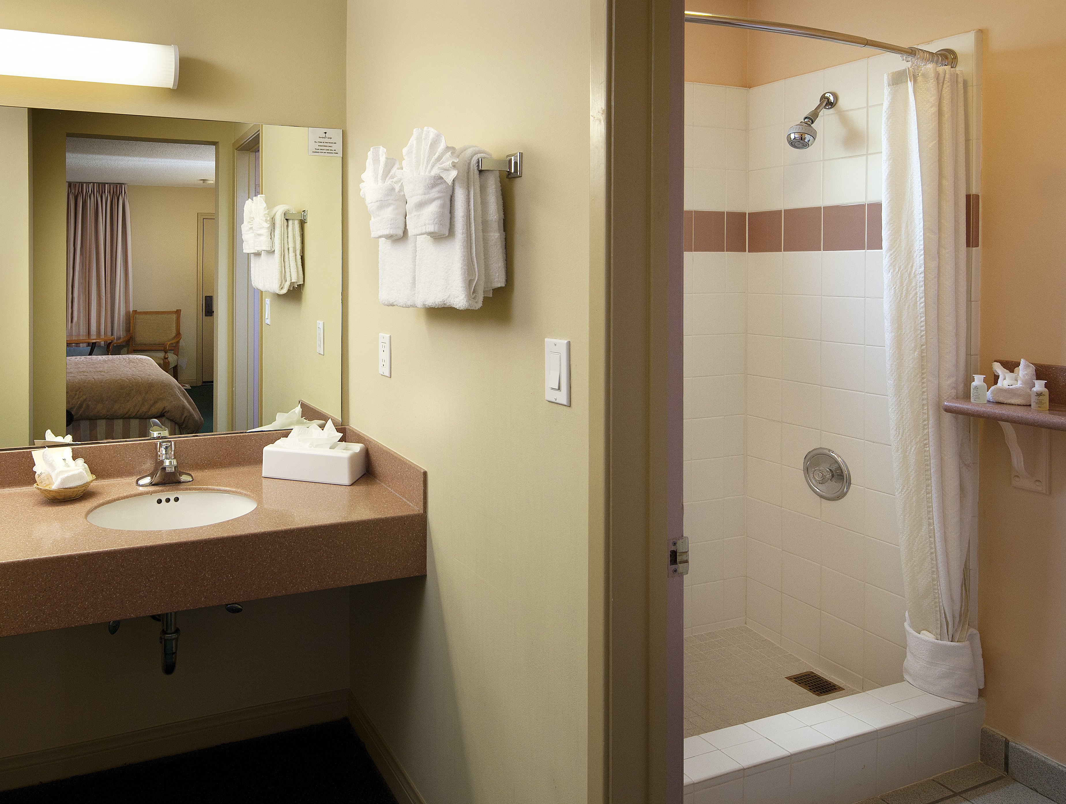 A bathroom with a sink, mirror, towels, and shower.